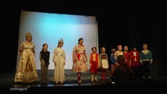 Viele verkleidete Kinder stehen bei einer Probe am Bühnenrand in einer Reihe nebeneinander. © Screenshot 