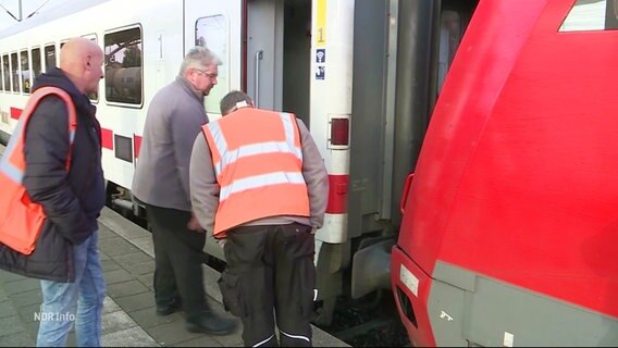 Drei Bahnbeamte betrachten die Verbindung zwischen Lok und Waggons. © Screenshot 