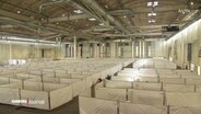 Mit Bauzäunen und Planen in einer Halle der Messehallen abgetrennte Bereiche für eine Flüchtlingsunterkunft (Archivbild). © Screenshot 