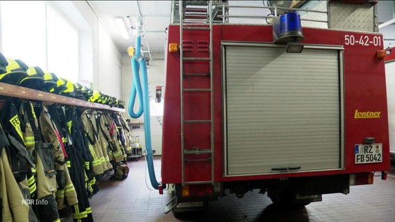 Ein Feuerwehrauto neben Einsatzbekleidung. © Screenshot 