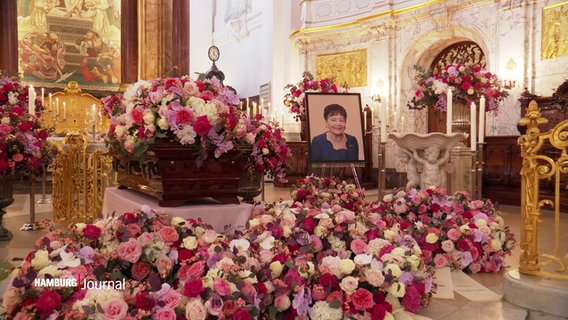 Ein Foto der verstorbenen Hannelore Greve, umrahmt von Blumenschmuck zur Trauerfeier im Hamburger Michel. © Screenshot 