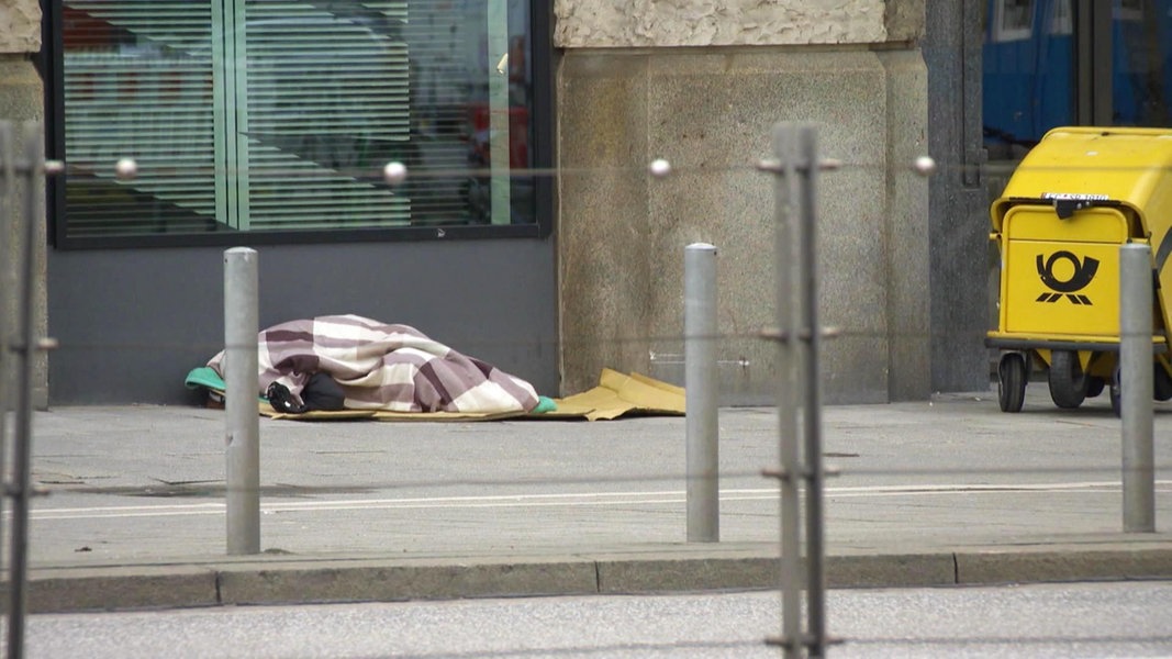 Ein obdachlose Person liegt auf der Straße unter einer Decke.