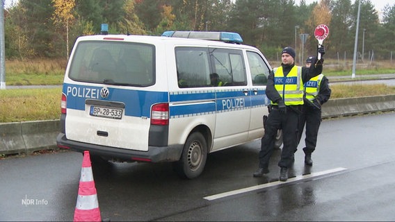 Polizisten der Bundespolizei auf einer Straße, neben ihnen ein Polizeiwagen. Ein Polizist hält eine rote Kelle hoch. © Screenshot 