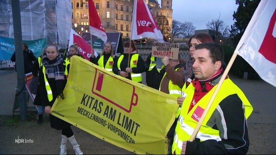 Kita-Beschäftigte demonstrieren in Wahnwesten und mit Fahnen auf einer Demo für höheren Lohn. © Screenshot 