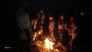Eine Gruppe junger Pfadfinder steht an einem Lagerfeuer. © Screenshot 
