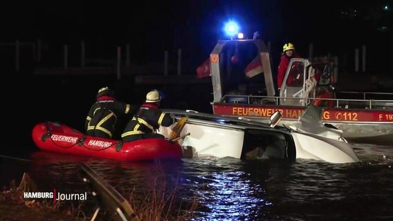 Einsatzkräfte der Feuerwehr versuchen einen auf der Seite liegenden Kleinwagen in der Alster über kleine Boote zu bergen. © Screenshot 