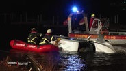 Einsatzkräfte der Feuerwehr versuchen einen auf der Seite liegenden Kleinwagen in der Alster über kleine Boote zu bergen. © Screenshot 