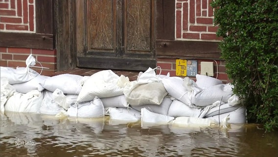 Vor einer Haustür liegen mehrere Schichten Sandsäcke um umliegendes Hochwasser abzuhalten. © Screenshot 