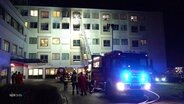 Ein Feuerwehrauto mit Blaulicht steht vor dem Helios Klinikum Uelzen. Eine Leiter führt zu den vom Brand betroffenen Stockwerken. © Screenshot 