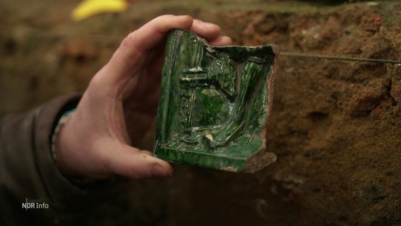 Ein Archäologe hält ein Ausgrabungsstück in der Hand. © Screenshot 