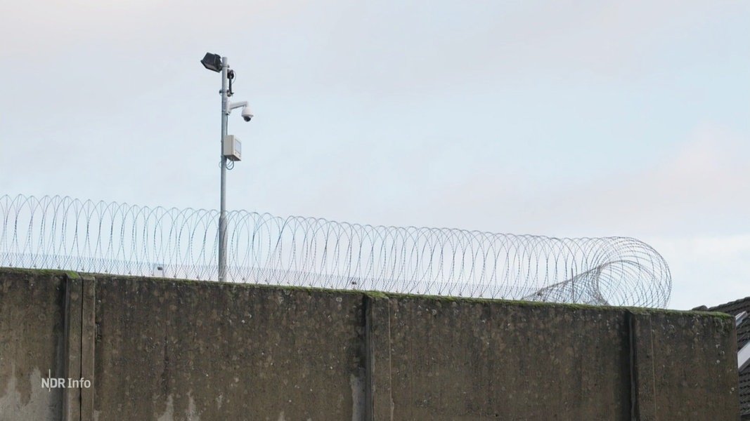 Eine Gefängnismauer mit Stacheldraht und einer Flutlichtanlage.
