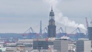 Der Turm des Hamburger Michel, umgeben von höhren Gebäuden, im Hintergrund die Kräne des Hafens und eine Rauchsäule eines Fabrikschlotes. © Screenshot 