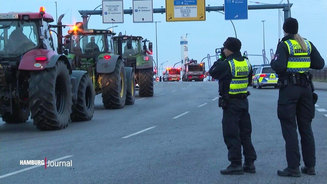 Polizisten sehen auf einer Autobahn stehend den abrückenden Bauern in ihren Trekkern zu.