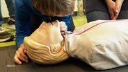 Beim Erste-Hilfe-Kurs: Eine junge Person hat den Kopf über eine Puppe gebeugt um zu spüren, ob der "Patient" atmet. © Screenshot 