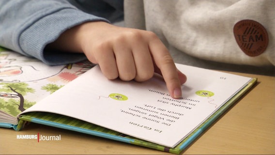 Eine Kinderhand fährt mit einem Finger an einem Text in einem Buch für Lese-Anfänger entlang. © Screenshot 