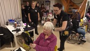Anja Voigt, Organisatorin der Aktion "Barber Angels Brotherhood", hält nach dem Haareschneiden einen Spiegel neben den Hinterkopf ihrer Kundin, einer älteren Dame. © Screenshot 