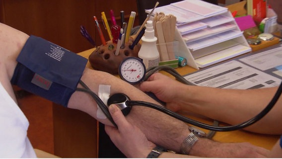 Ein Hausarzt misst am Arm eines Patienten den Blutdruck. © Screenshot 