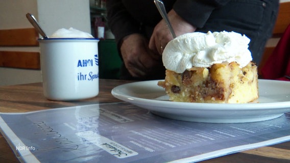 Ein Stück Apfelkuchen mit Sahne und ein Becher Kaffee © Screenshot 
