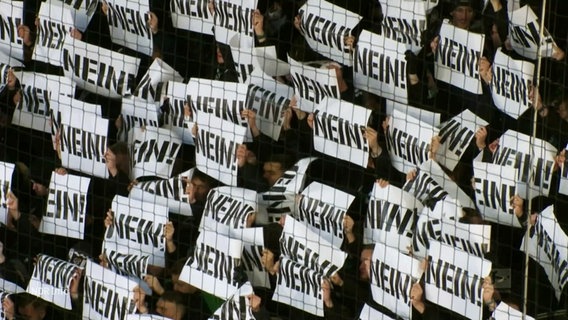 Fußballfans halten Zettel mit der Aufschrift „Nein“ in die Höhe. © Screenshot 