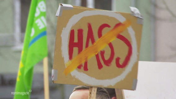 Auf einem selbstgebastelten Schild steht das Wort "Hass", das durchgestrichen ist. © Screenshot 
