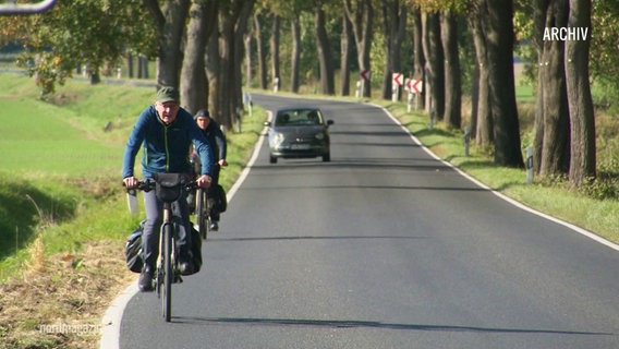 Menschen mit Fahrrädern auf einer Landstraße. © Screenshot 