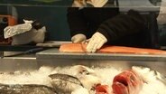 An einer Fischverkaufstheke wird ein Lachs geschnitten. © Screenshot 