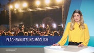 Nachrichtensprecherin Lilli Michaelsen im Studio, links von ihr ein Bild von einem Festival und darunter der Titel "Flächennutzung möglich". © Screenshot 