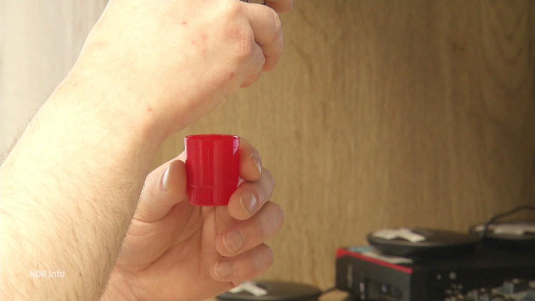 Ein Pfleger füllt ein Medikament in einen kleinen roten Plastikbecher.