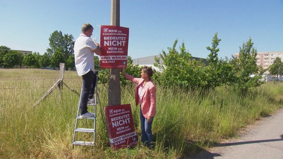 Zwei Personen hängen Wahlplakate der Bürgerinitiative Greifswald auf. © Screenshot 