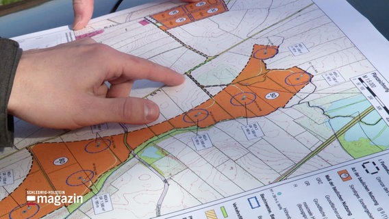 Eine Hand zeigt auf eine Fläche auf einer schematischen Landkarte mit teilweise orange eingefärbten Bereichen. © Screenshot 