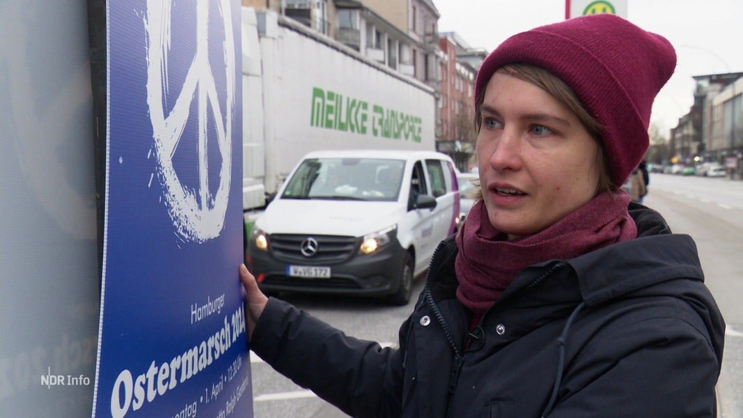 Eine Frau steht vor einem Plakat zum Ostermarsch.