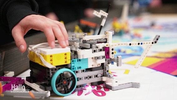 Eine Hand berührt einen bunten Mini-Roboter aus Lego. © Screenshot 