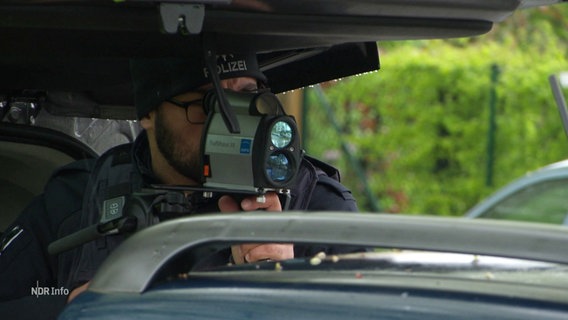 Ein Polizist blickt durch ein Gerät, dass die Geschwindigkeit von Objekten misst. © Screenshot 