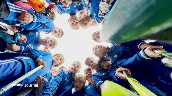 Junge Hockeyspieler schauen von oben herab, im Kreis stehend  in die Kamera. © Screenshot 