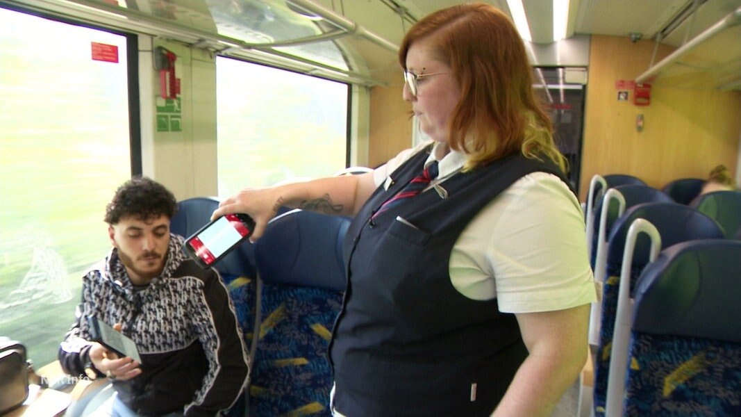 Eine Zugbegleiterin kontrolliert das Ticket eines Reisenden.
