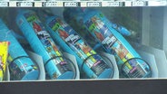 Bunt bedruckte Dosen mit Lachgas liegen in einem Snackautomaten. © Screenshot 