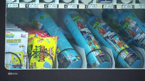 Mehrere Dosen mit Lach·gas liegen in einem Automaten. Der Automat hat auch Süßigkeiten. © Screenshot 