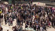 Schülerinnen und Schüler versammeln sich auf einem Platz. Einige tragen Fahnen oder Schilder bei sich. © Screenshot 