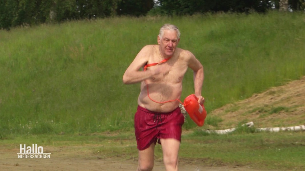 Der 76-jährige Rettungsschwimmer Klaus Kläres sprinted mit einer roten Rettungsboje in einen Badesee.