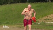 Der 76-jährige Rettungsschwimmer Klaus Kläres sprinted mit einer roten Rettungsboje in einen Badesee. © Screenshot 