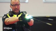 Ein Polizeibeamter mit Schutzbrille betätigt einen Elektroschocker. © Screenshot 