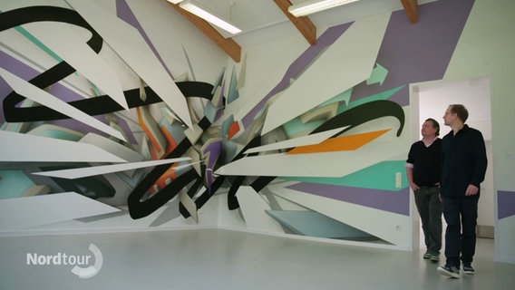 Der Kunstsammler Rik Reinking und der Künstler DAIM getreten einen Raum mit einem bunten Wandgemälde. © Screenshot 