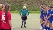 Herbert Schönbeck steht als Schiedsrichter zwischen zwei Jugend-Mädchenteams. Er ist ein Mann über 80, mit grauem und schütterem Haar. © Screenshot 
