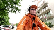 Der Lieferando-Fahrer Thomas sitzt in orangefarbener Dienst-Jacke auf seinem Fahrradd. © Screenshot 