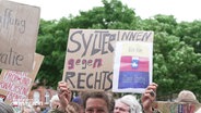 Blick über die Köpfe von Menschen hinweg, die Schilder empor halten. Auf einem steht "SylterInnen gegen Rechts". © Screenshot 