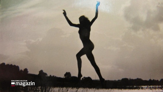 Schwarz, weiße Fotografie. Die schwarze Silhouette eines nackten Frauenkörpers springt in freier Natur. © Screenshot 