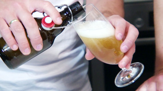 Nahaufnahme zeigt, wie eine Person Bier aus einer Bügelflasche in ein Glas einschenkt. © Screenshot 