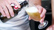 Nahaufnahme zeigt, wie eine Person Bier aus einer Bügelflasche in ein Glas einschenkt. © Screenshot 