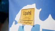 Ein gelber Aufkleber mit der Aufschrift "Upahl #nichtgefragt" auf blauem Hintergrund © NDR 