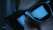 Ein Bildschirm spiegelt sich in einer Sonnenbrille auf dem Gesicht einer Person. © Screenshot 